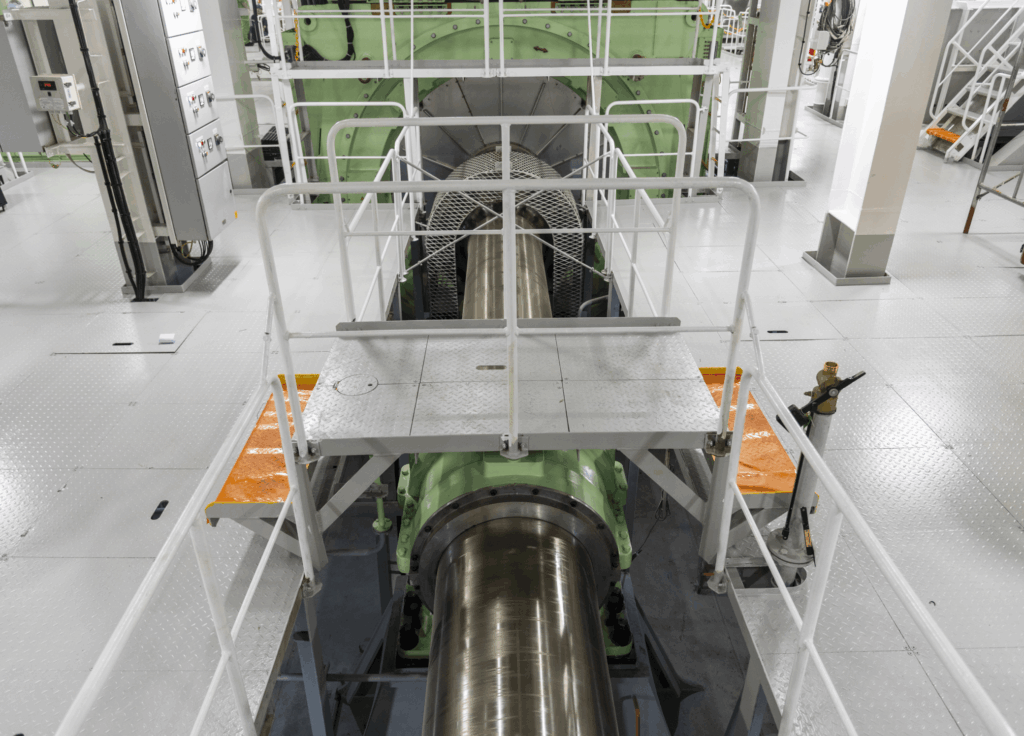 Carbon and alloy steel forged propulsion shaft connecting to a marine reduction gear in an engine room.